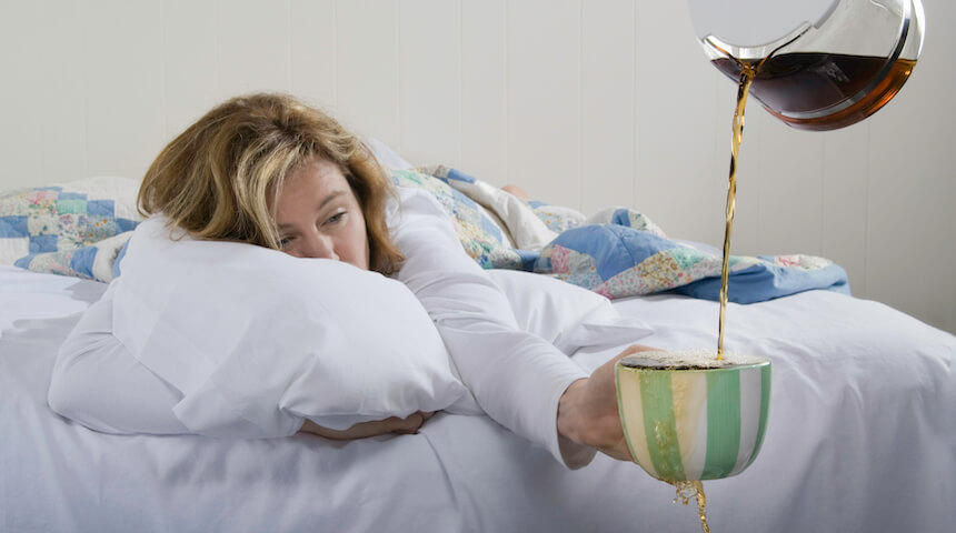 Tired woman in bed reaching out holding an overflowing cup of coffee being poured for her