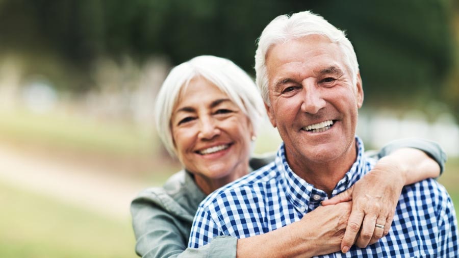 elderly woman with arms around husband