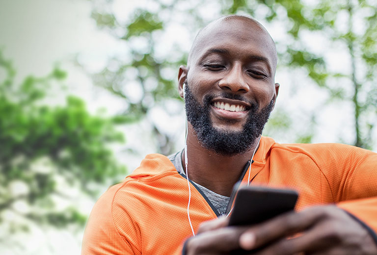 man wearing earbuds outside looking at smart phone