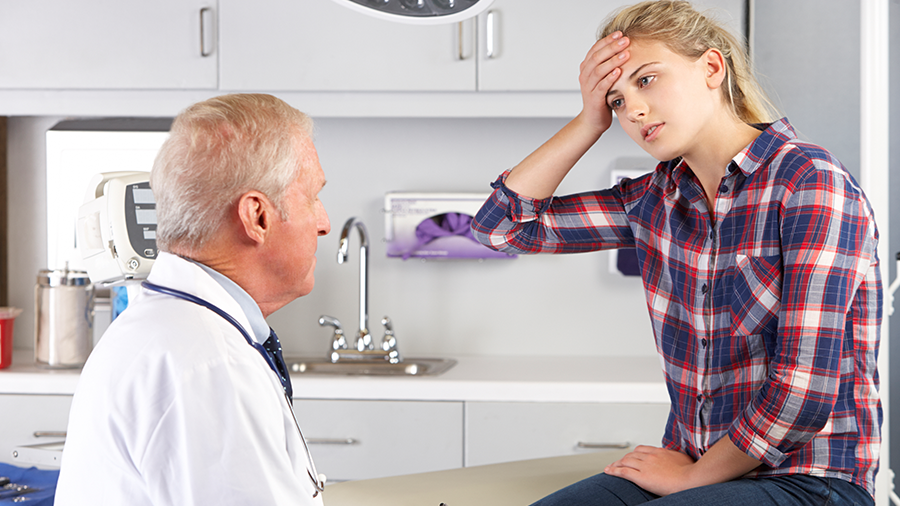 Young woman holding head in consultation with physician 