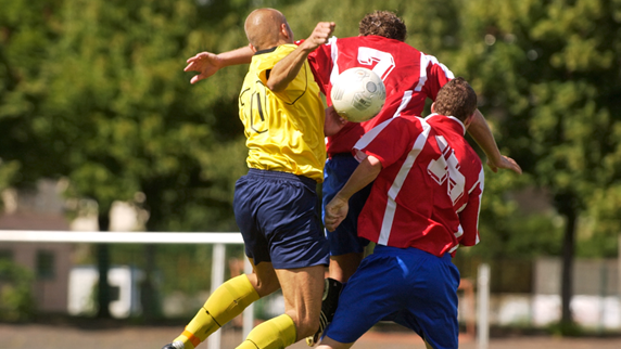 Three soccer players colliding on soccer field.