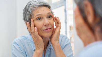 Older woman looking at her face in a mirror.