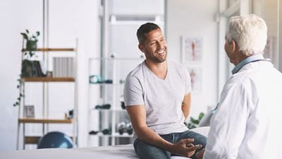 male patient speaking to doctor while sitting on examination table