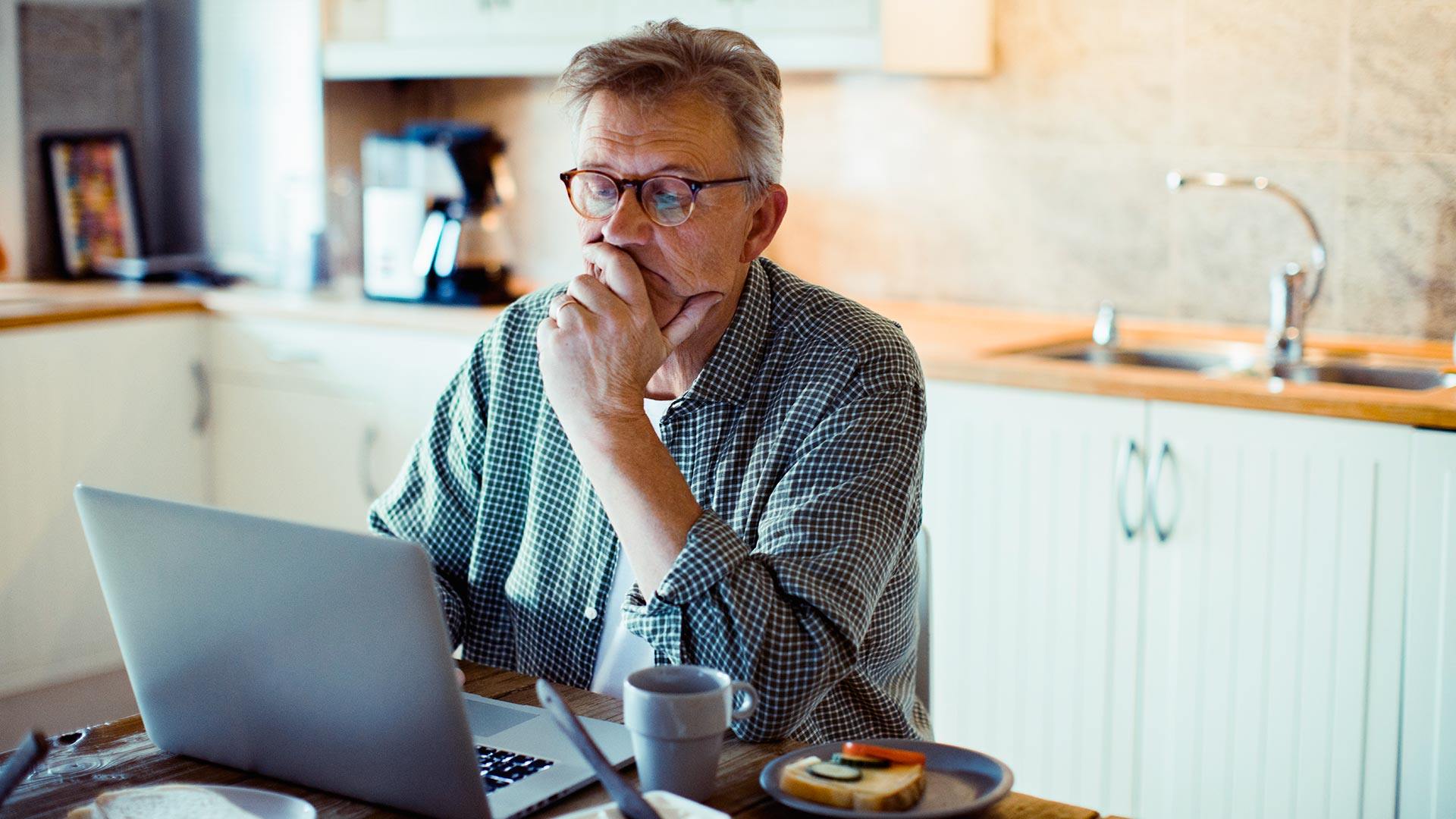 Close up of a mature man using a laptop at home while having breakfast