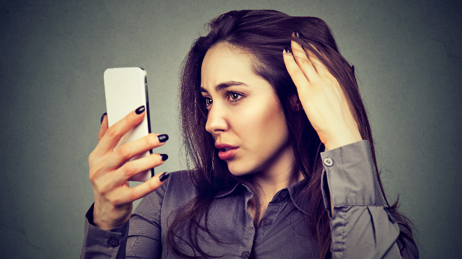 A woman looking at her receding hairline in the reflection of her cell phone.