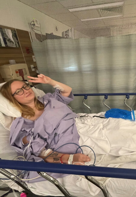 Girl in hospital bed throwing up a peace sign