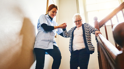 A home health care professional helping her patient down the stairs.