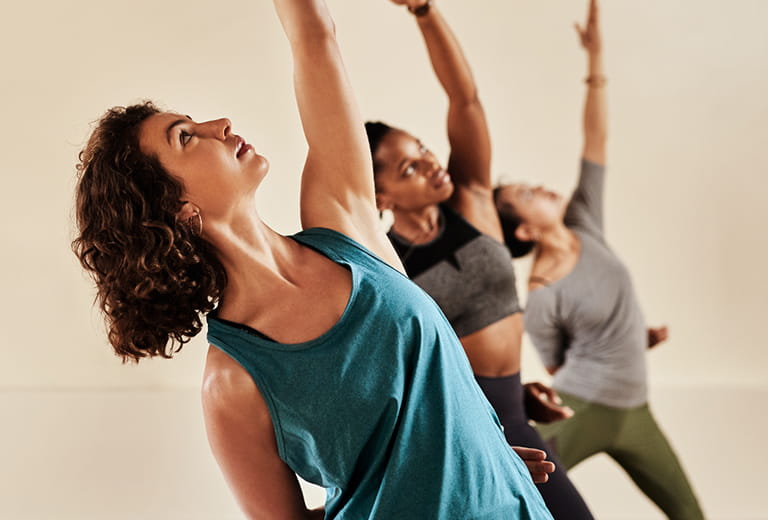 three women stretching with hands toward the ceiling