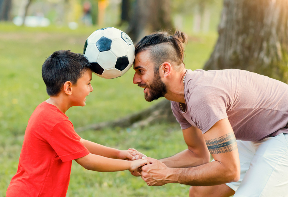 man with child holding a soccer ball between their heads
