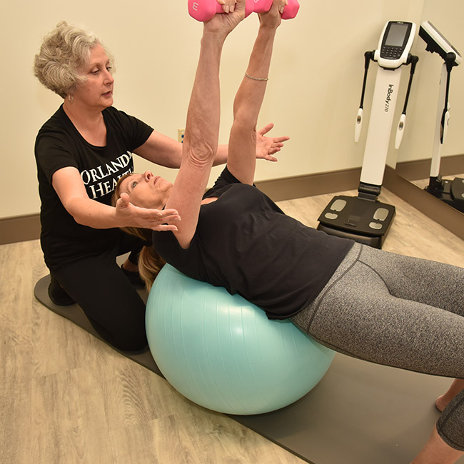 Trainer helping participant with exercise ball and dumbells