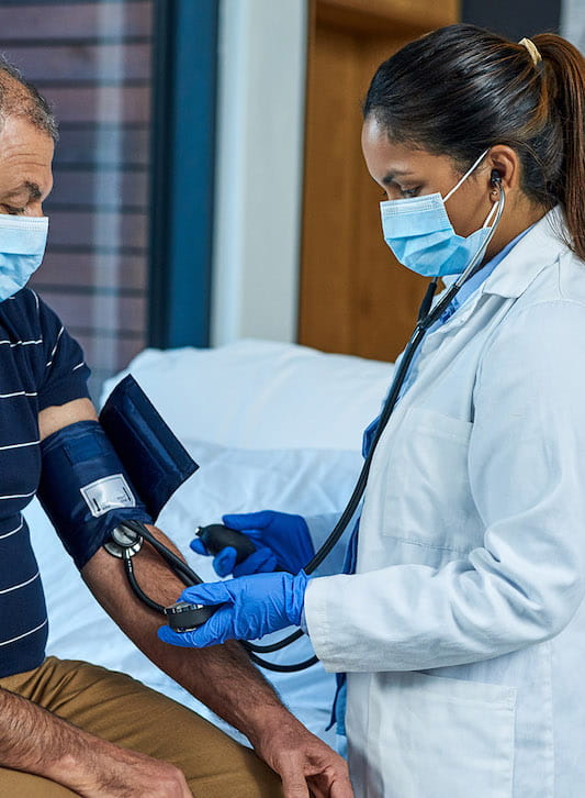 man sitting on bed getting blood pressure checked by doctor 533x726