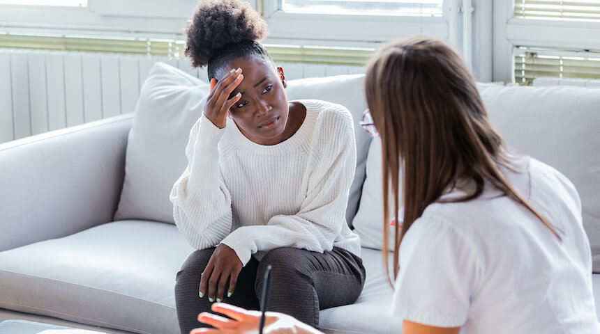 Woman holding head speaking with another woman