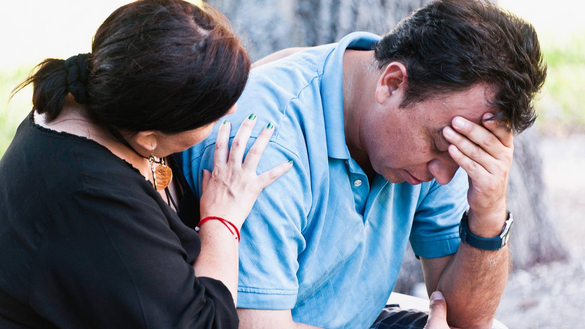 Hispanic mature couple sitting in a park bench, he is very concerned about his memory loss and she is consoling him with her arm around him