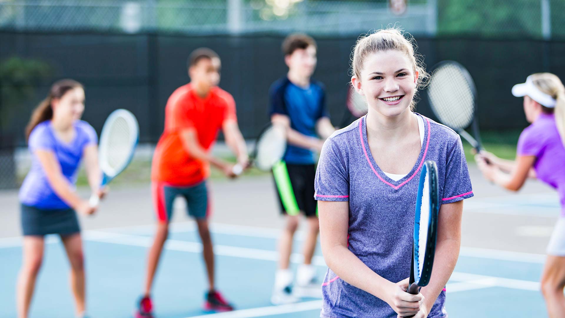 Multi-ethnic group of teenagers at tennis court with instructor.
