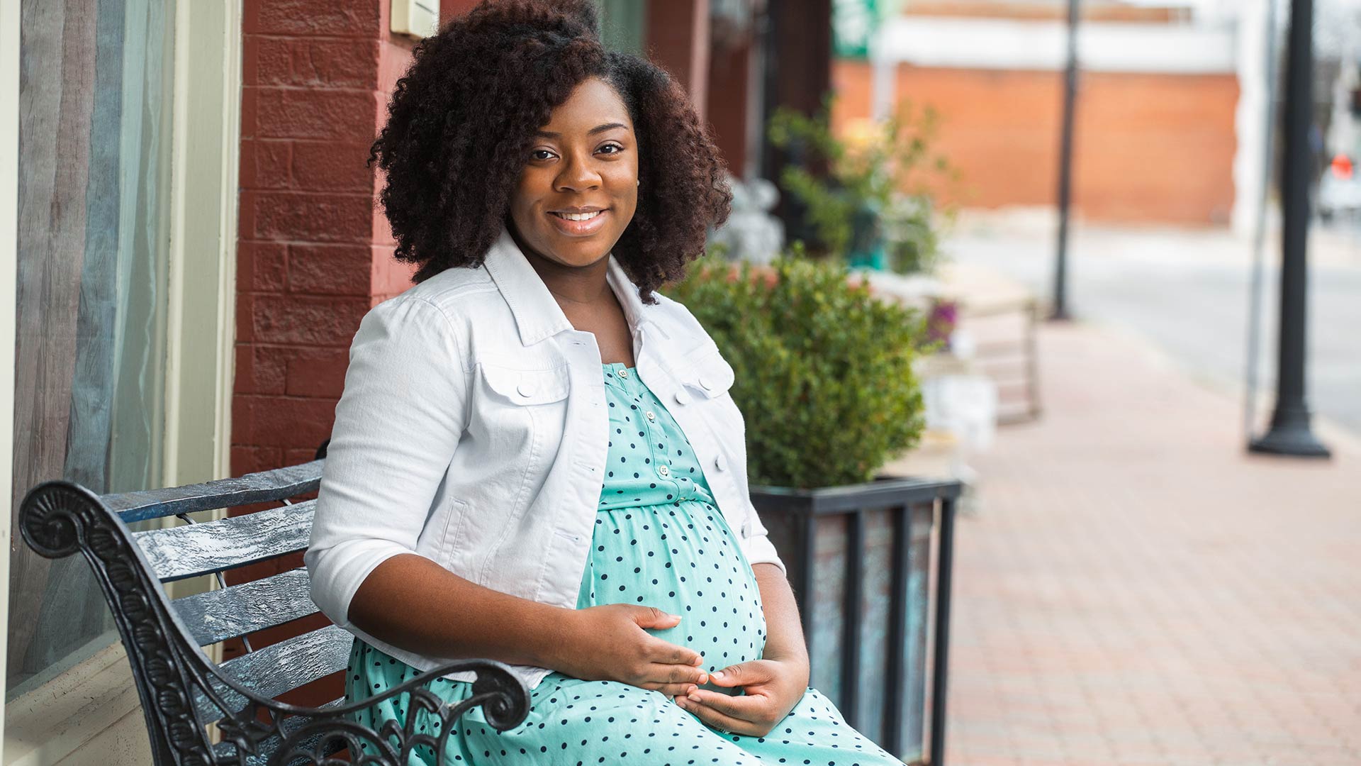 Young pregnant African American woman sitting on a bench smiling