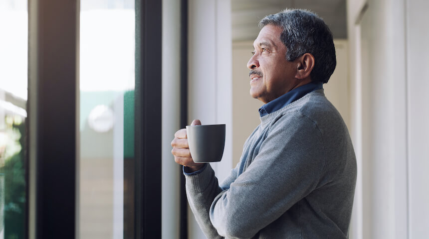 man holding mug while looking out through a window