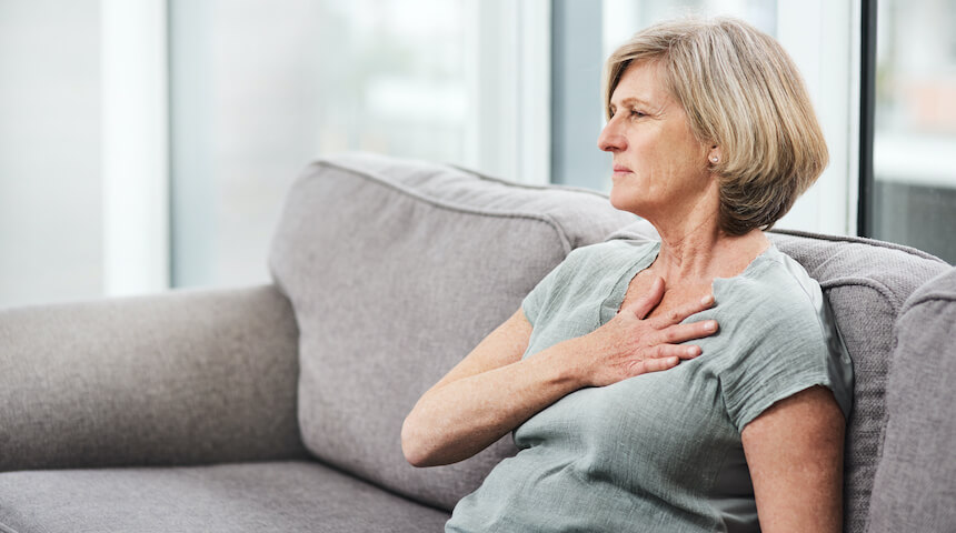 Woman sitting on couch with hand holding chest