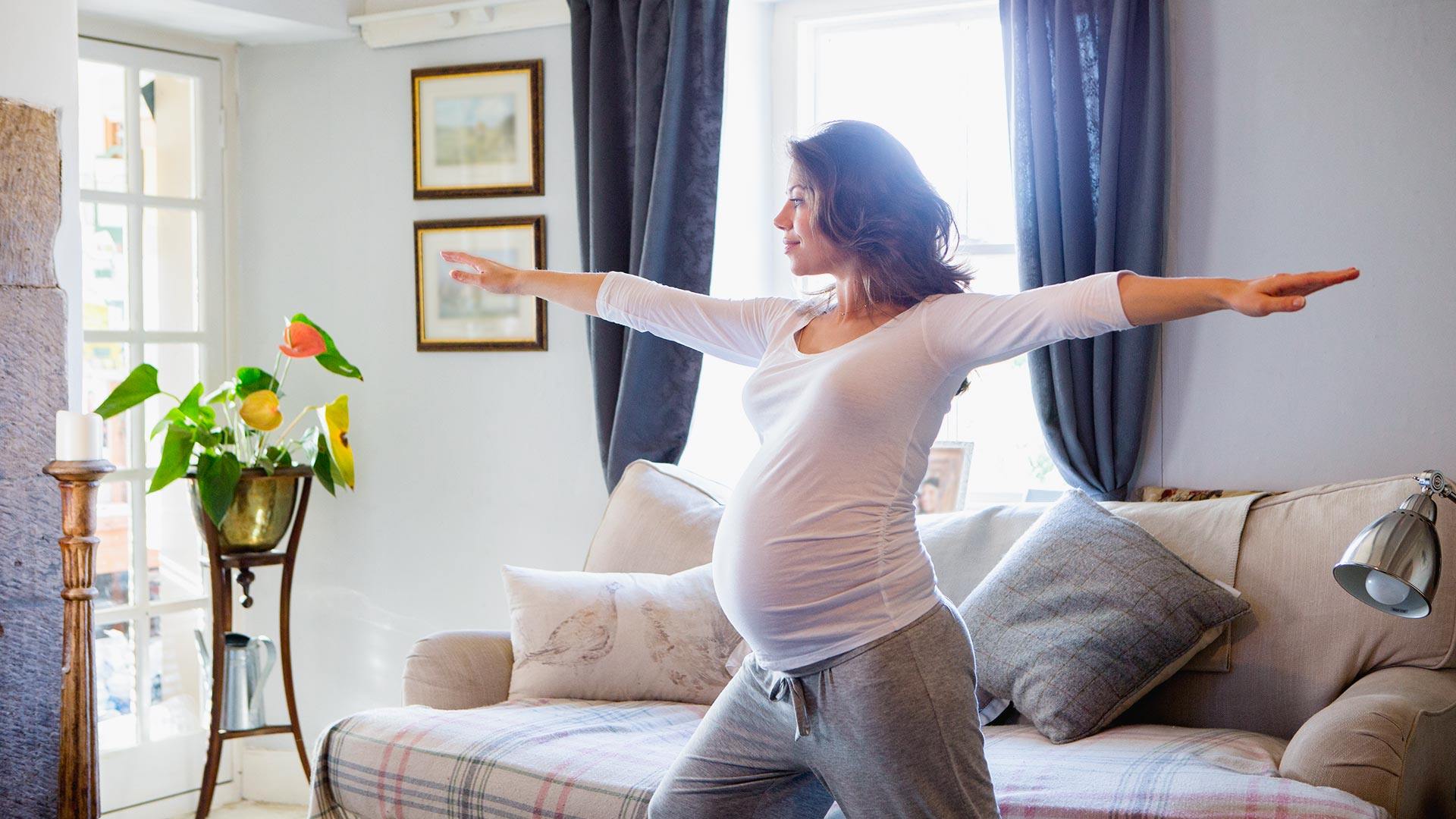 A heavily pregnant woman is exercising in her home.