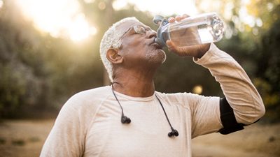 An older African American male drinking water outdoors after working out.