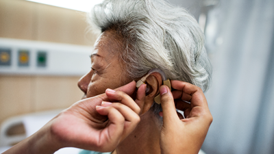Physician placing hearing aid into the ear of an older woman.