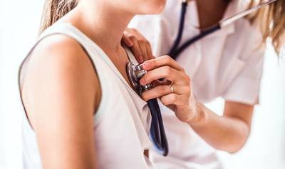 Female doctor using stethoscope to listen to heartbeat of female patient