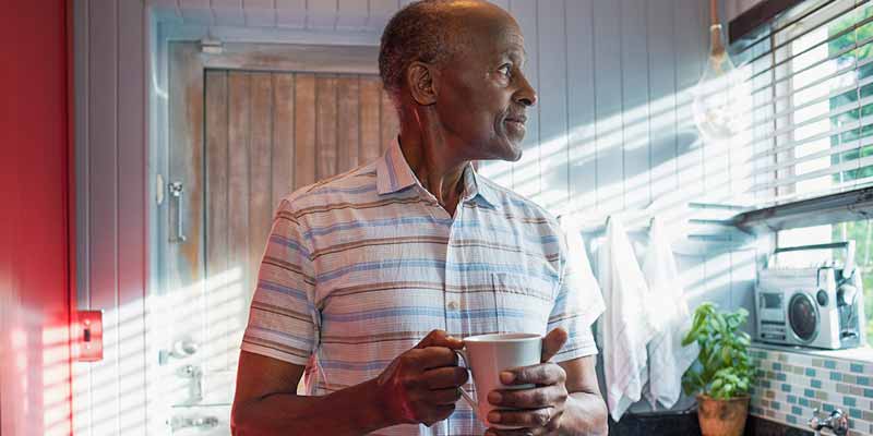 Man holding coffee cup looking thoughtfully out kitchen window